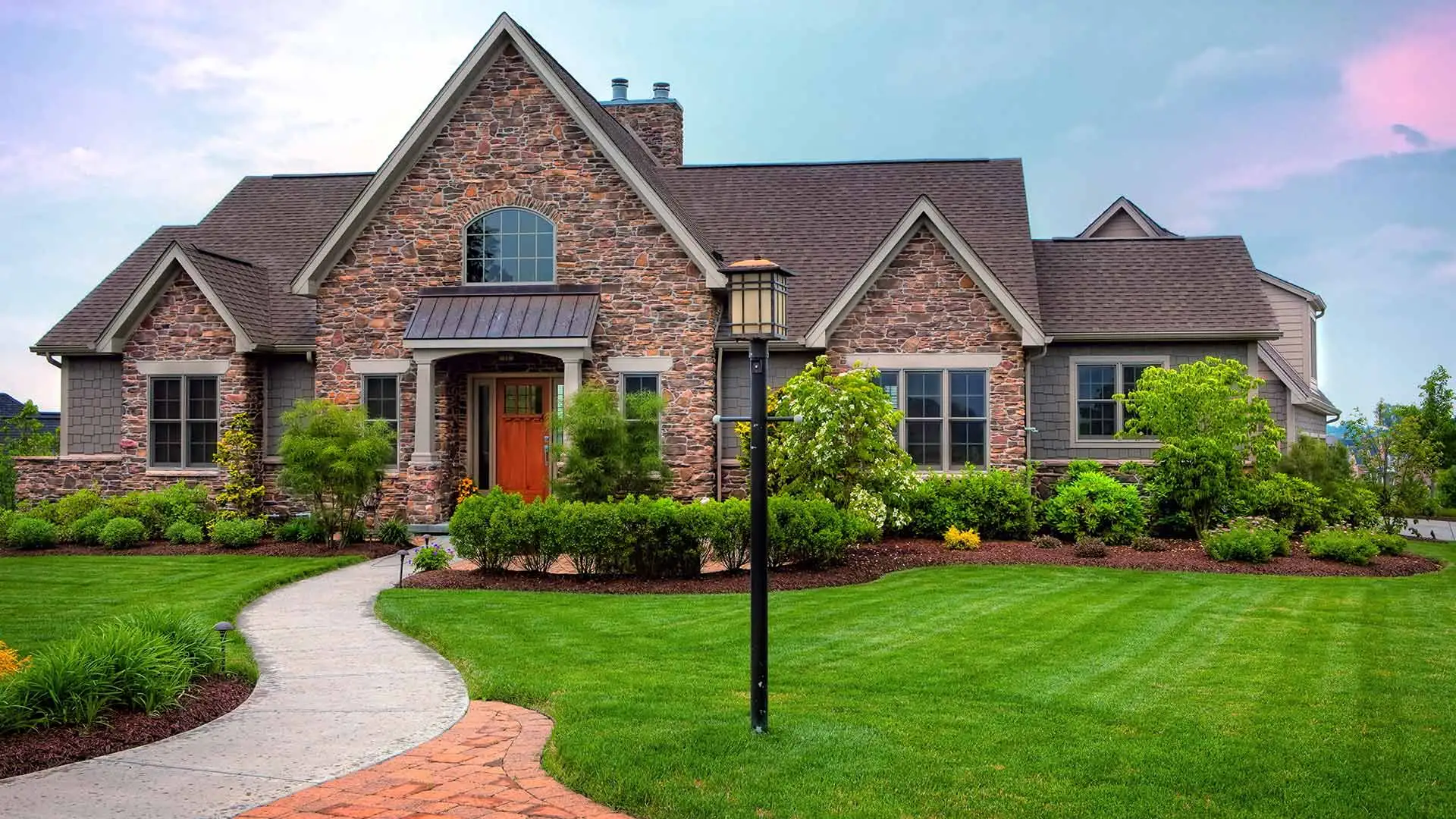 Lush lawn and shrubs on property with a cute stone home in Fairview, TX.